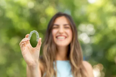 Woman holding up a clear aligner outdoors
