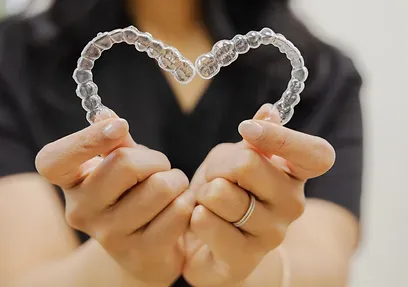 Hands holding two clear aligners in a heart shape at Ridgefield Orthodontics