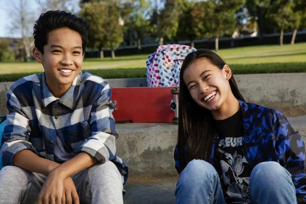Two smiling teenagers sitting outdoors at a park.