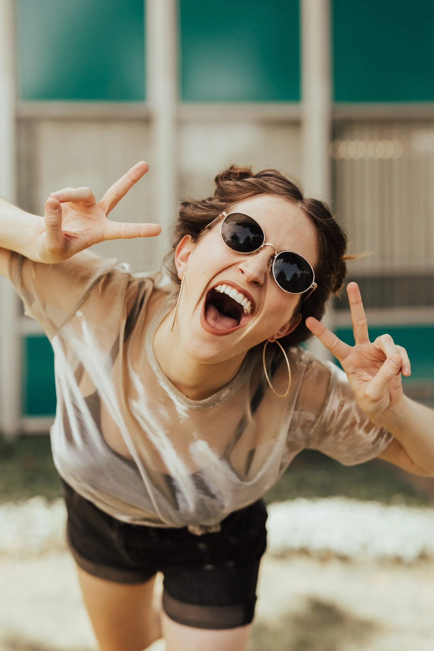 Laughing woman in sunglasses making peace signs with both hands.