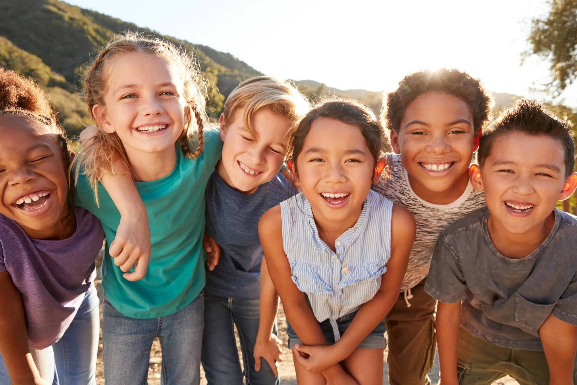 Group of smiling children with their arms around each other outdoors.