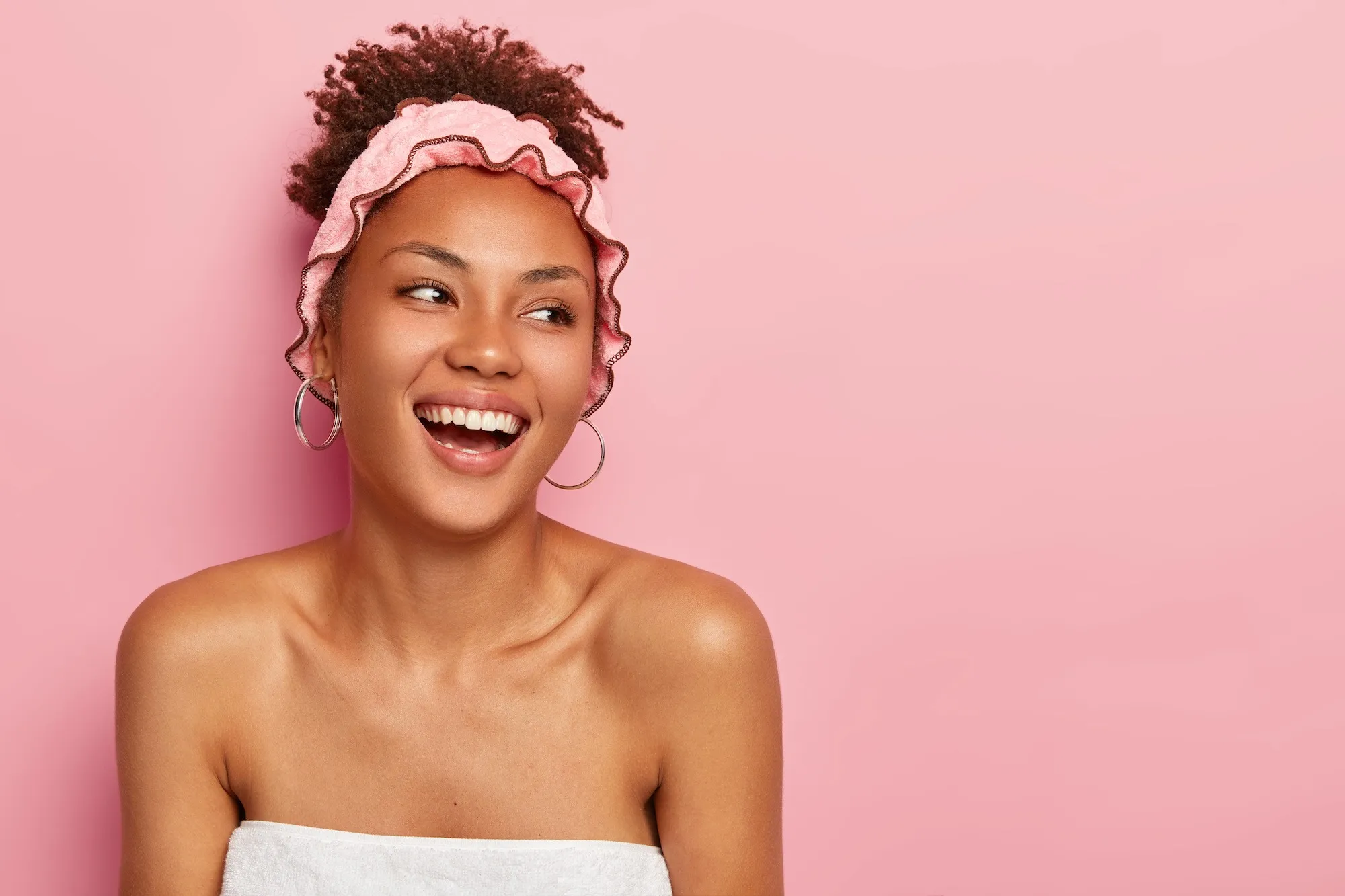 Smiling woman wearing a pink headband against a pink background.