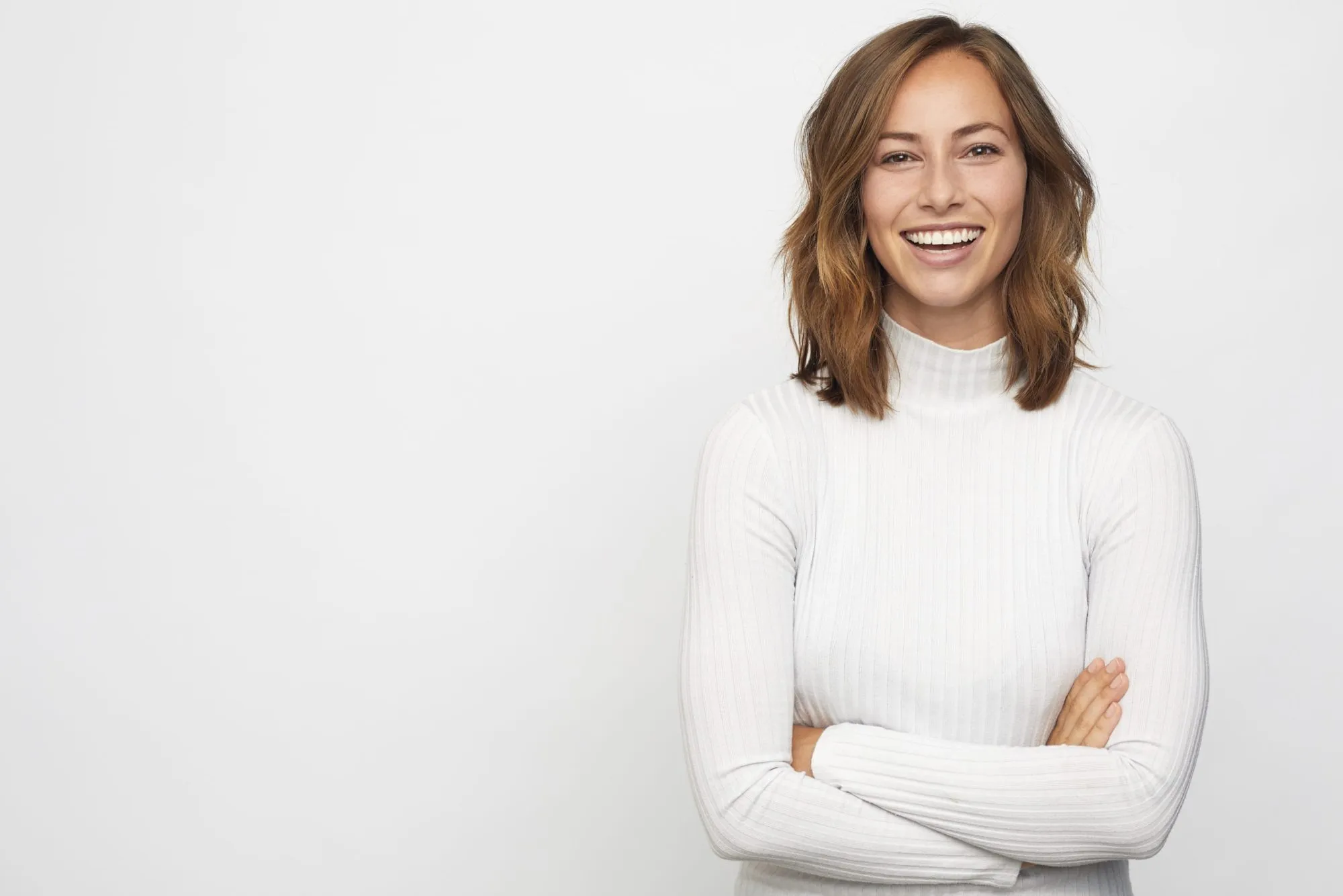 Smiling woman with brown hair wearing a white ribbed turtleneck with arms crossed.