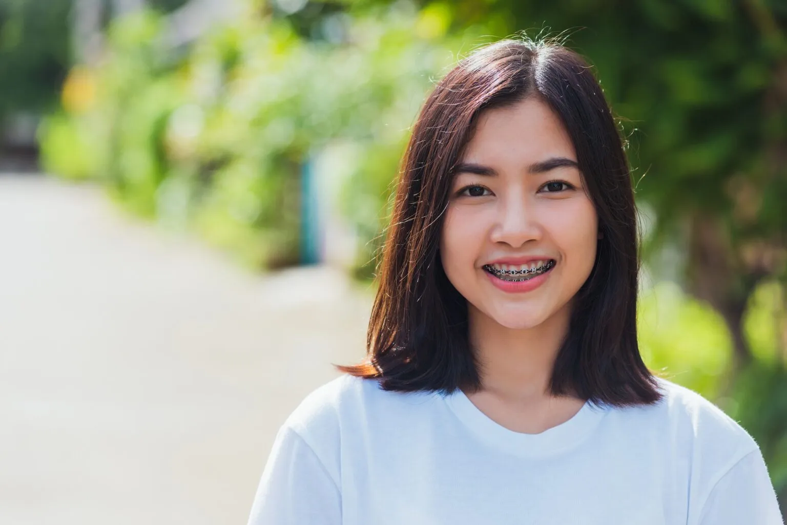 Smiling teenage girl with metal braces standing outdoors.
