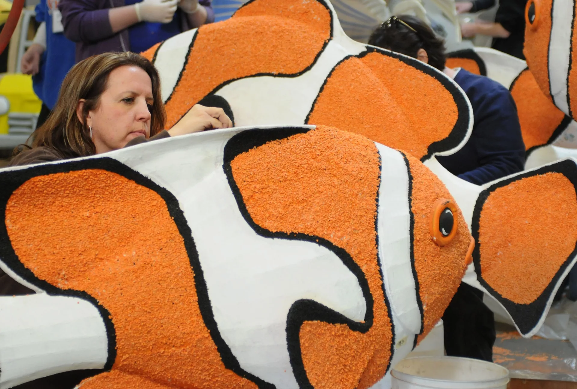 Artist crafting large orange and white clownfish sculptures with a textured surface.