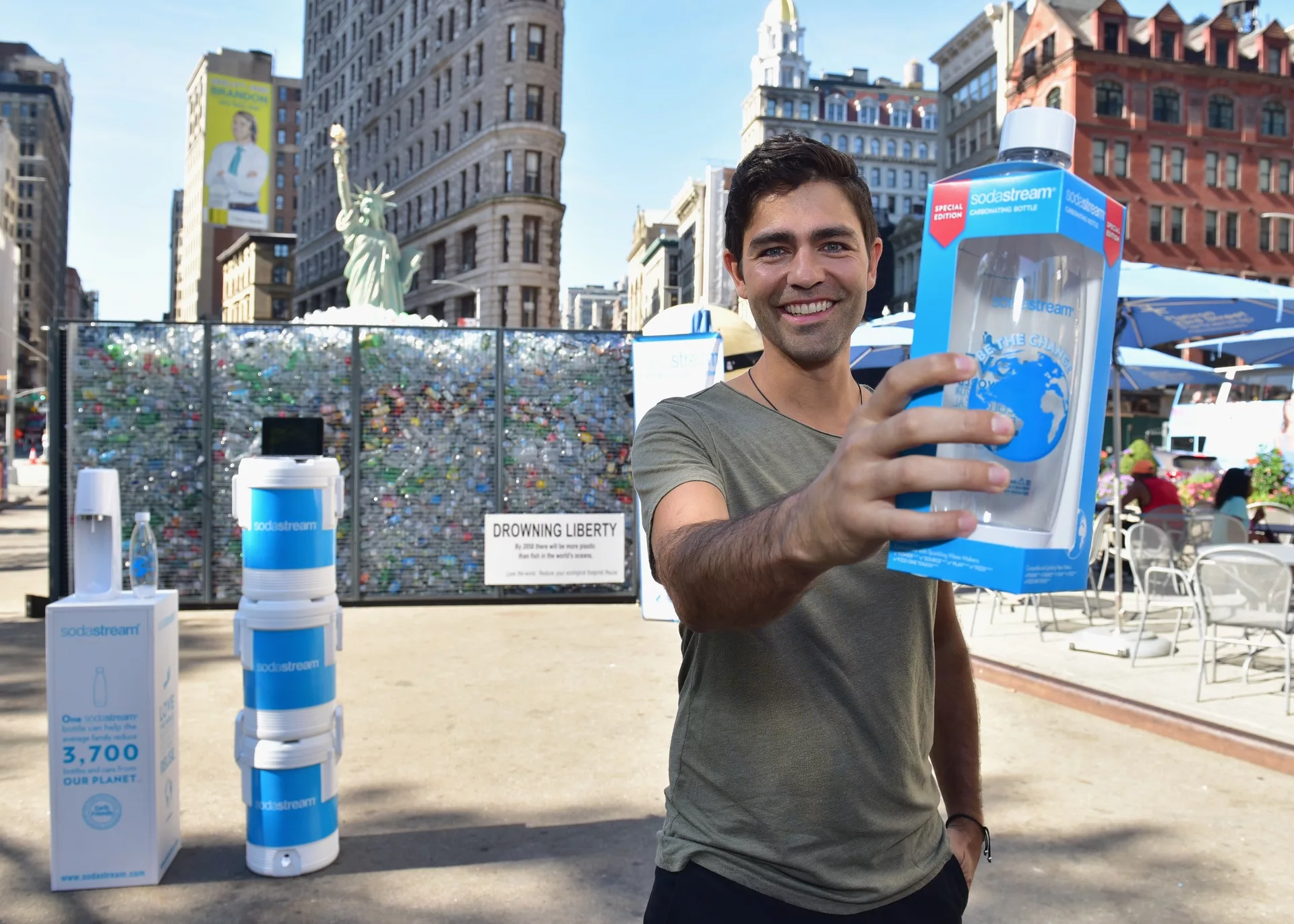 Man holding SodaStream bottle in front of plastic-filled Liberty statue backdrop at outdoor event