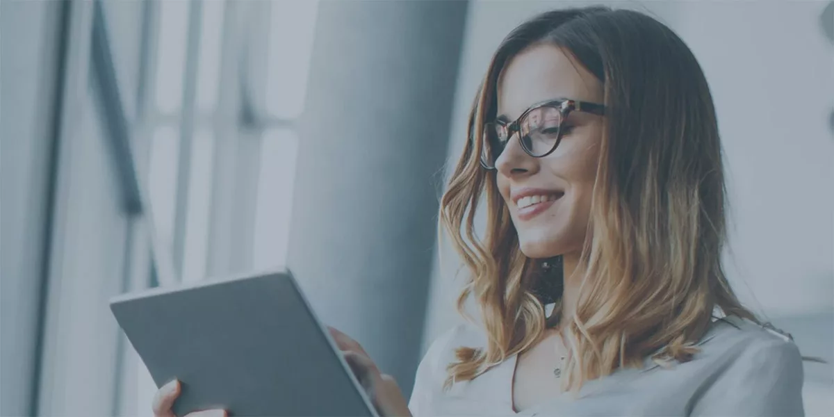 Smiling woman with glasses uses a tablet by a window
