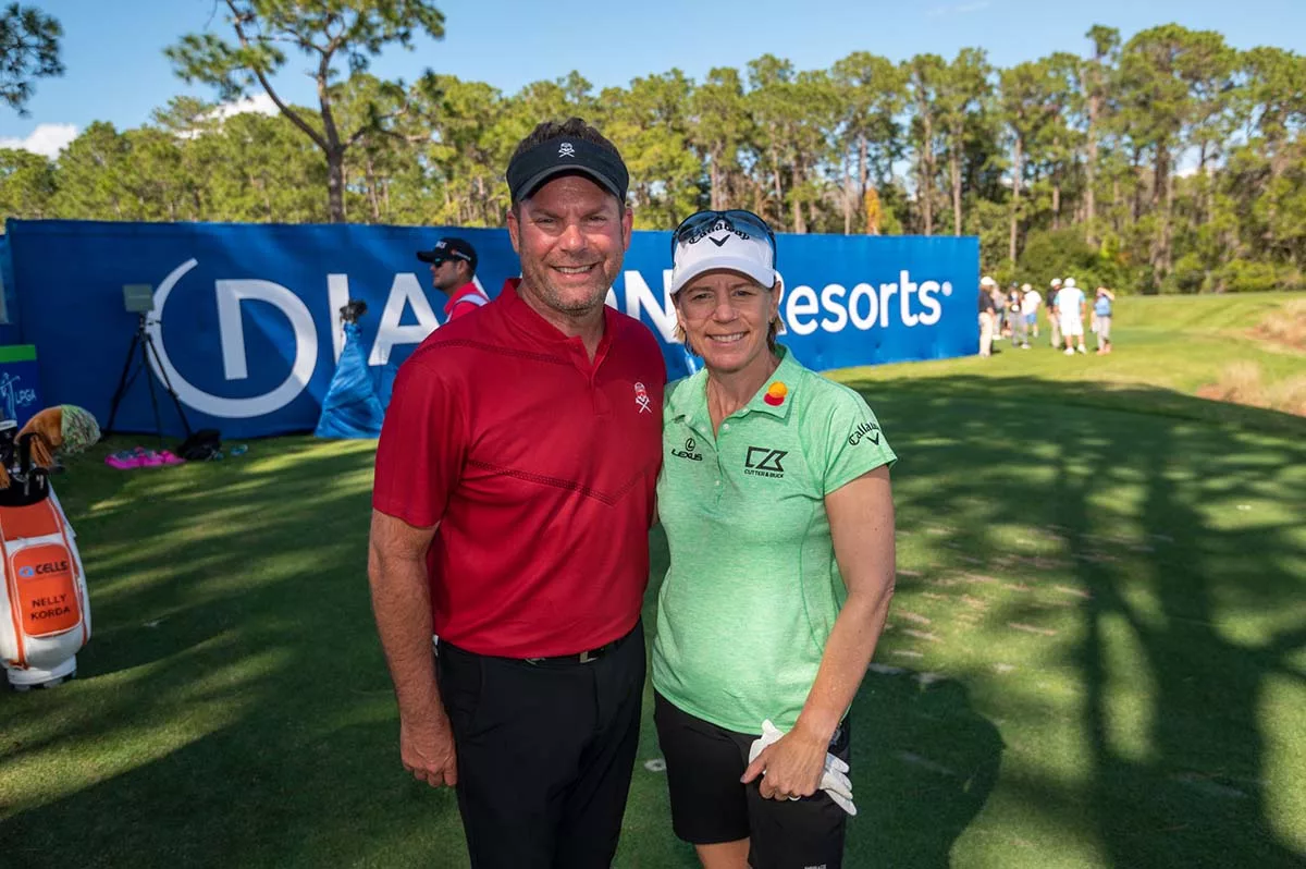 Two golfers smiling on a golf course with trees and a Danzante Bay Resorts sign in the background.