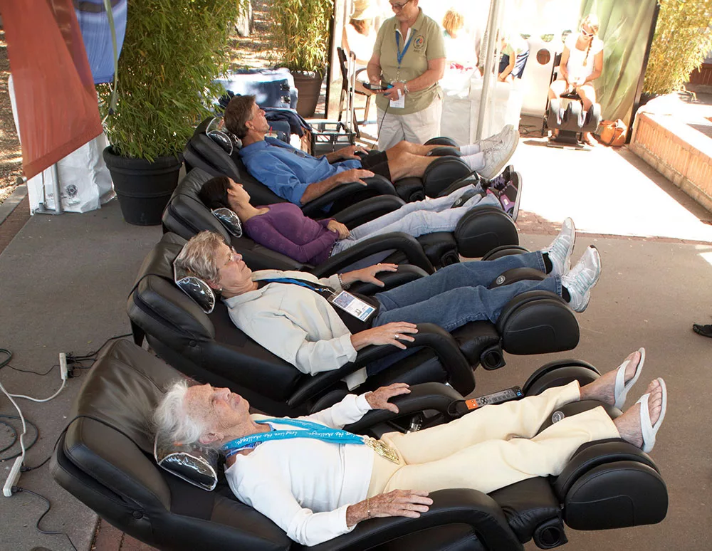 People relaxing on massage chairs outdoors at a wellness event.