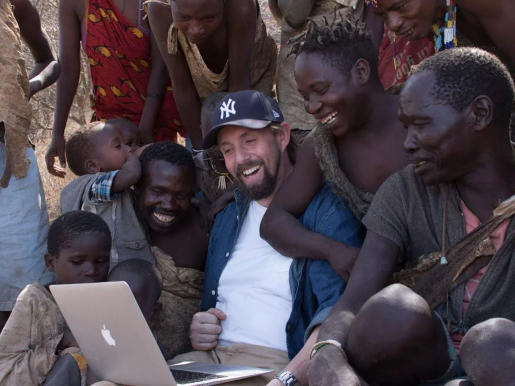 Group of people smiling and watching a laptop together outdoors