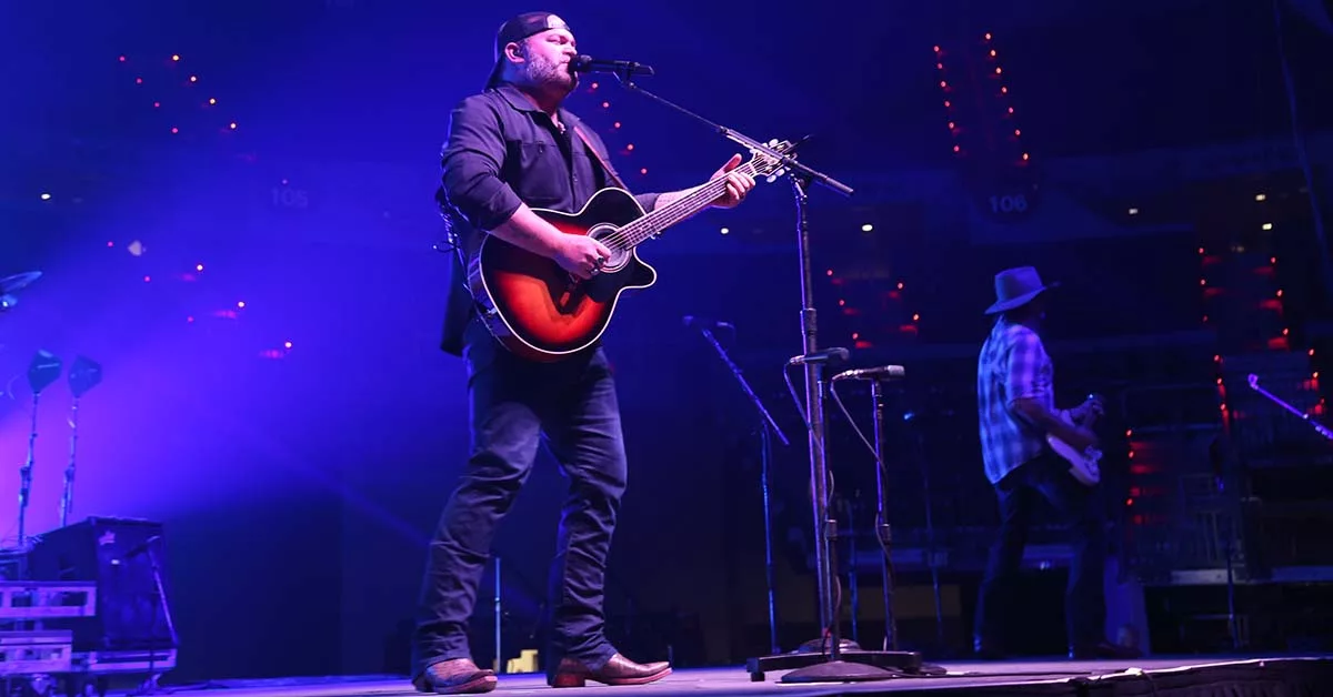 Guitarist sings on stage under purple lights in a lively concert setting