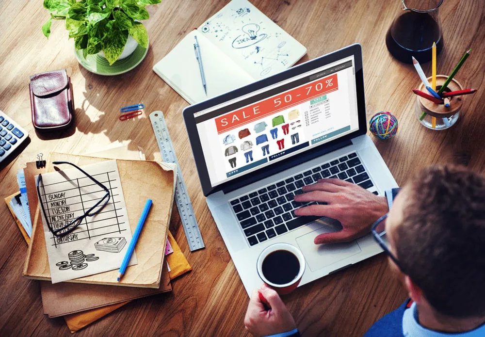Man shopping online for clothing deals on laptop with sale banner