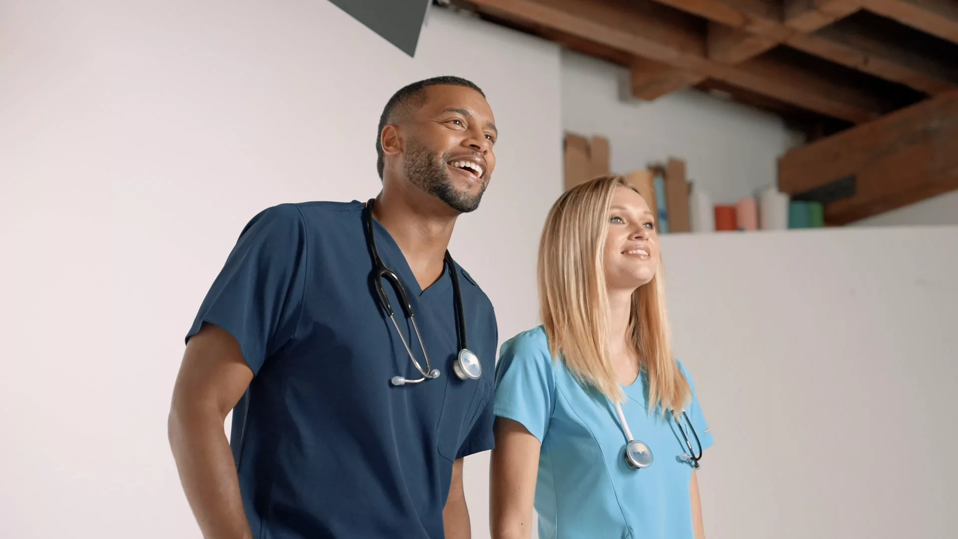 Two smiling doctors in blue scrubs and stethoscopes