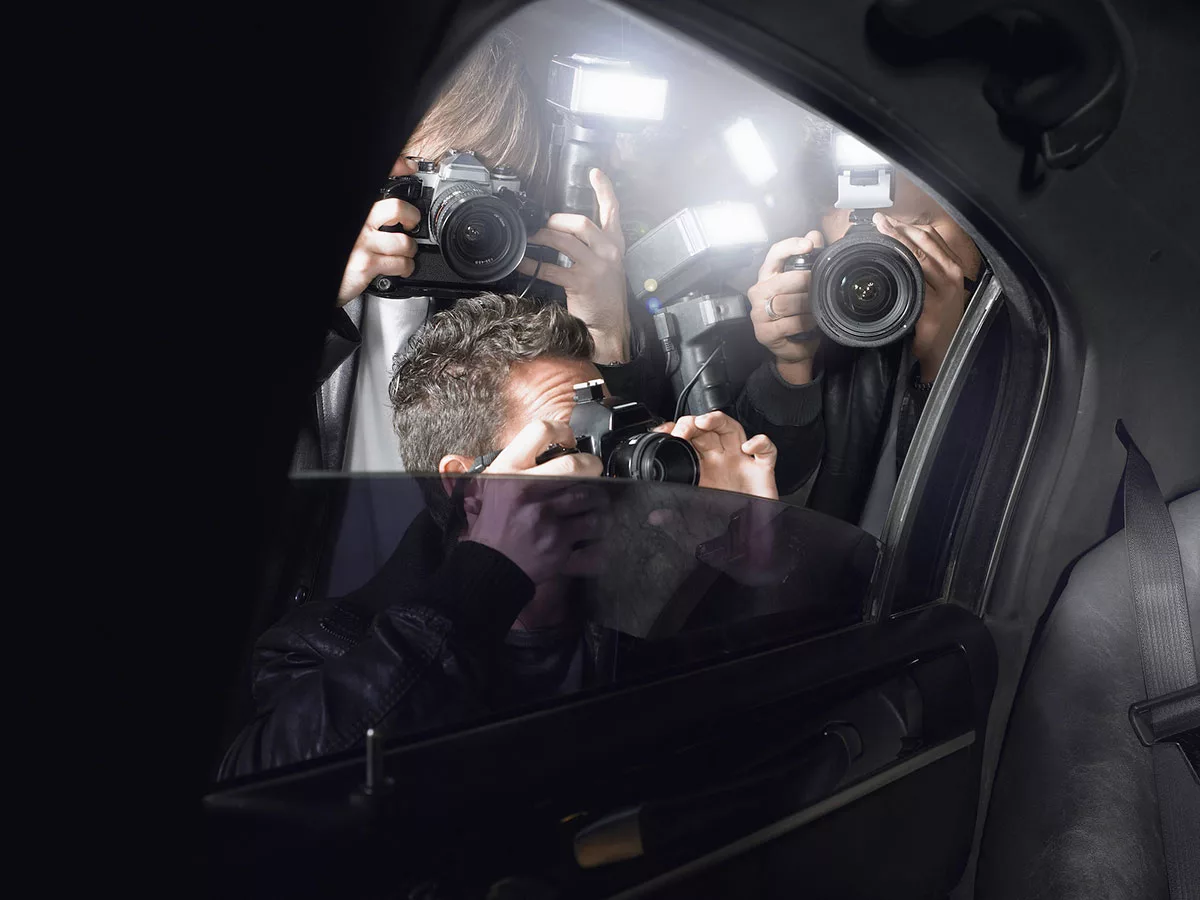 Photographers with cameras flash outside car window at night.