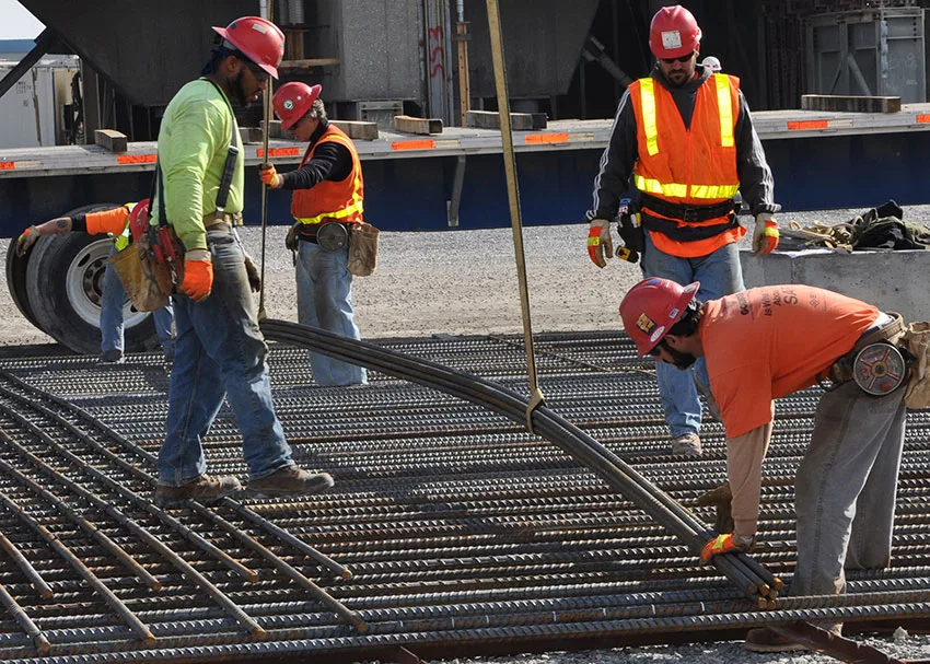 Construction workers in safety gear handling rebar at a building site