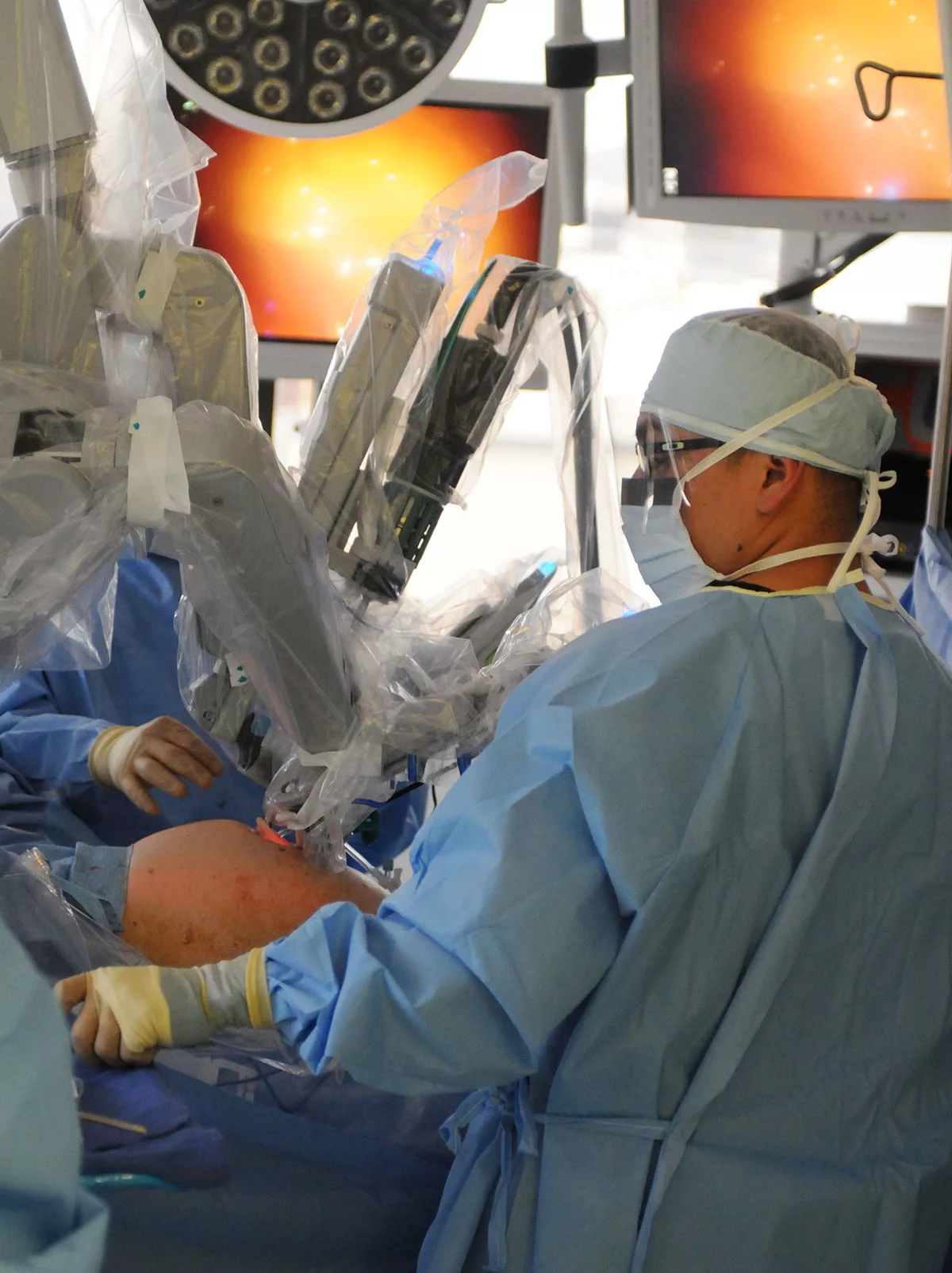 Surgeon operating robot in sterile hospital setting.