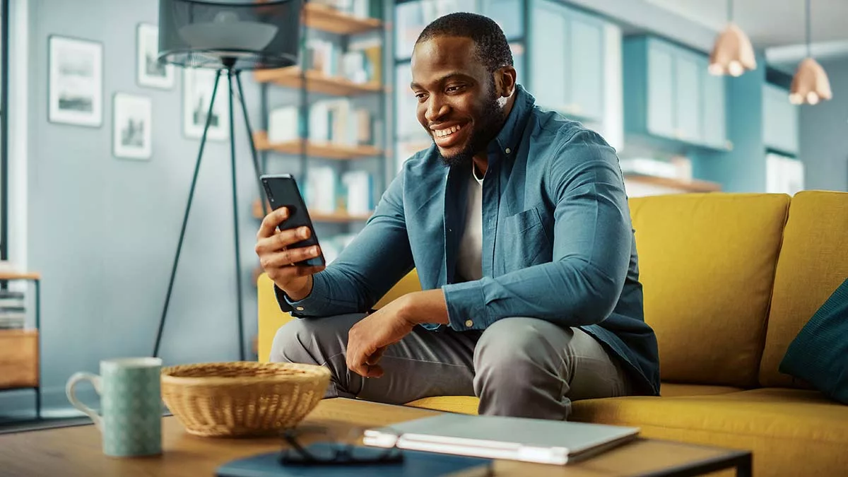 Man smiling at smartphone in modern living room with bookshelf and yellow couch.