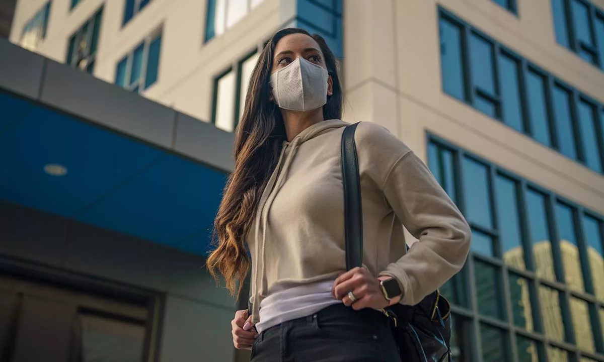 Woman in mask and hoodie stands outside modern building