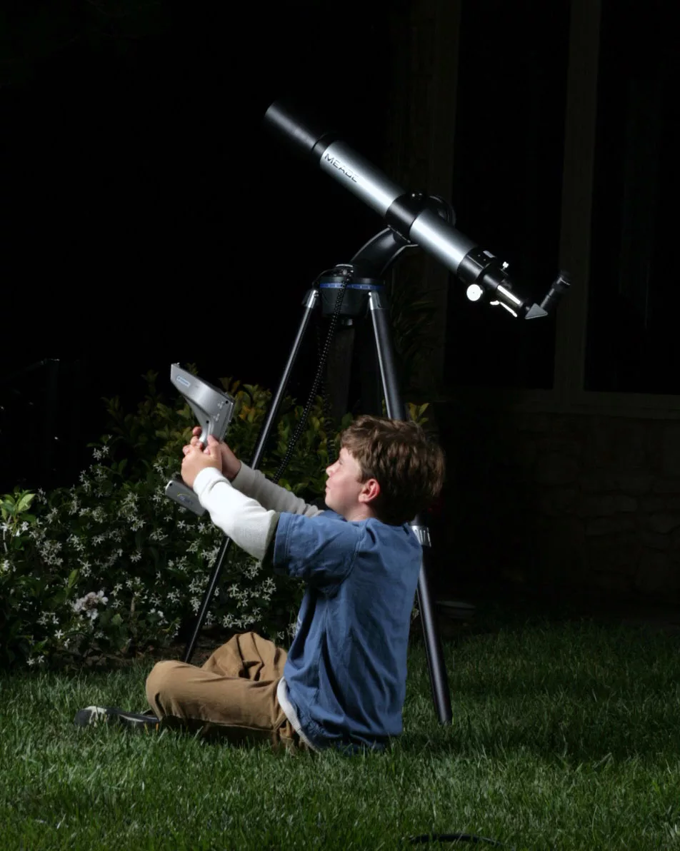 Child stargazing at night with a telescope on a grassy lawn.