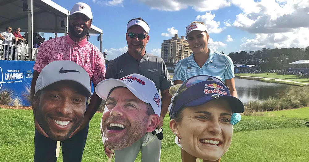 Golfers holding large cutout faces on a sunny golf course