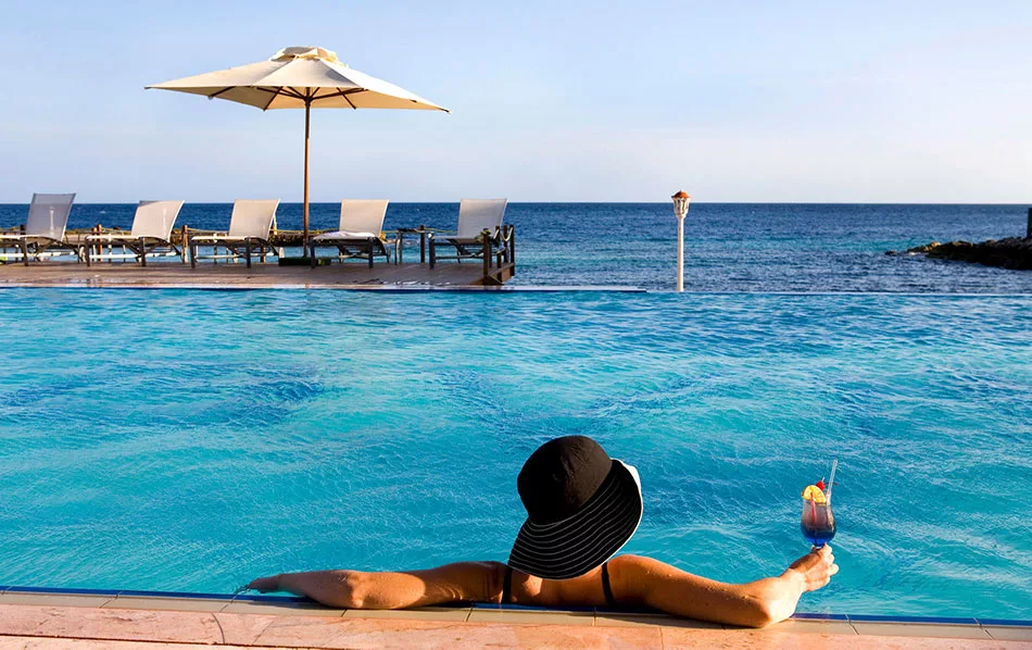 Woman in a black sunhat relaxes in an infinity pool