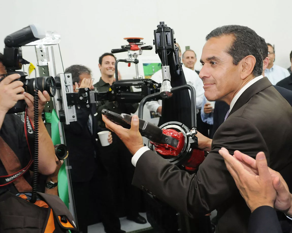 Man in a suit demonstrates industrial machinery to photographers at an event