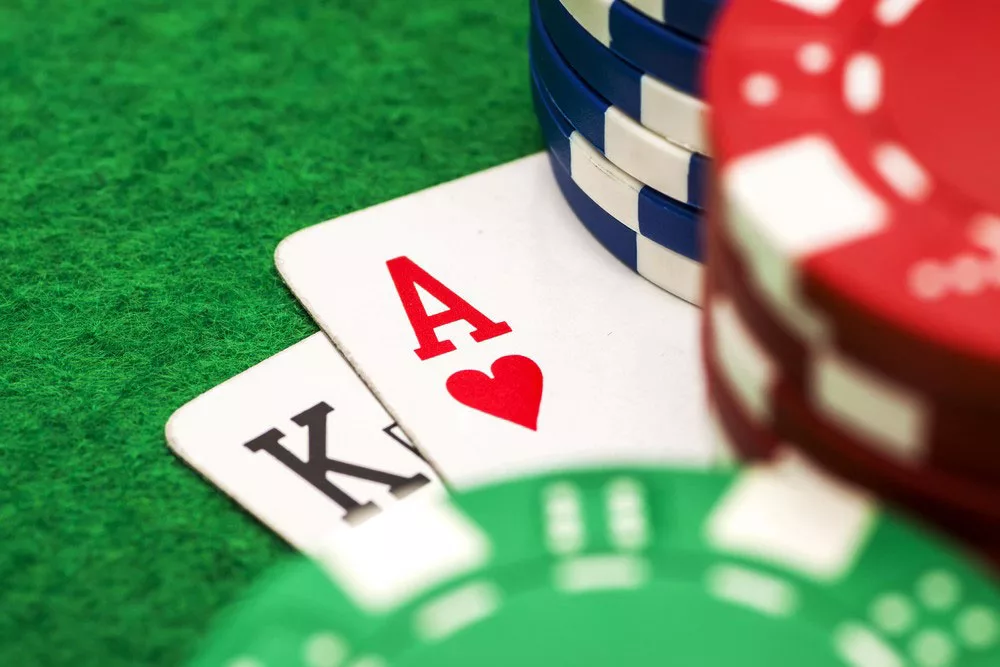 Ace of hearts and king of spades with poker chips on a green felt table.
