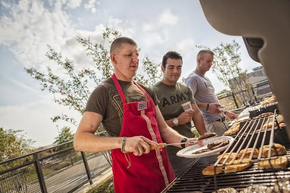 Three men grilling burgers and chicken outdoors on a sunny day.