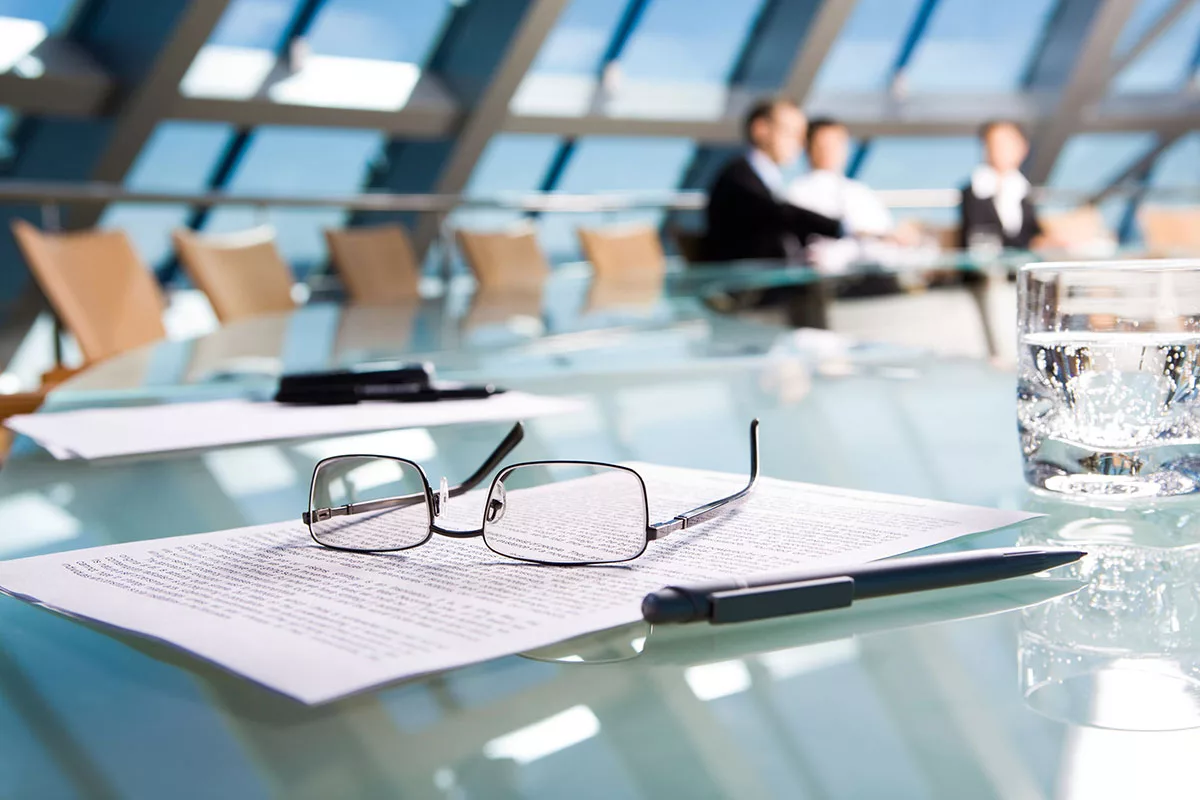 Glasses and pen on a document in focus with group meeting in background