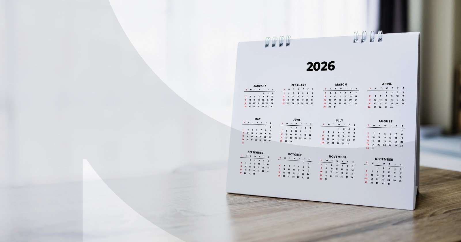 A 2026 calendar propped up on a wooden desk with a window in the background.