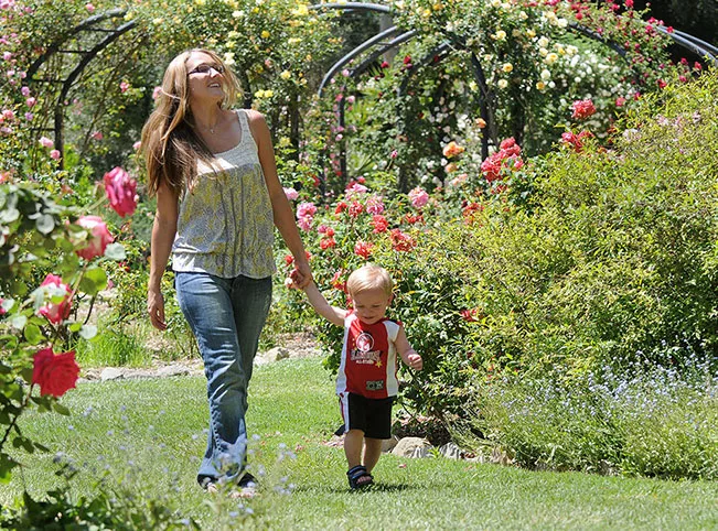Woman and child stroll through vibrant rose garden on a sunny day