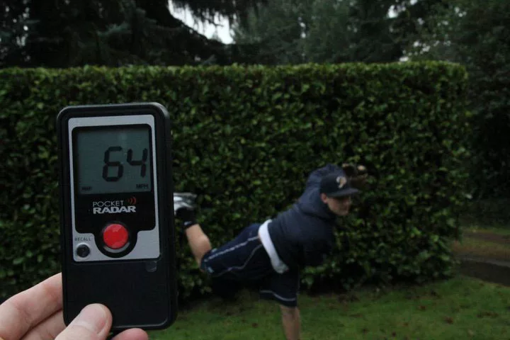 Radar gun showing 64 mph with a pitcher in motion against a green hedge background