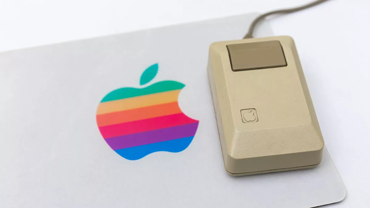 Vintage Apple mouse beside a rainbow-striped Apple logo on a laptop