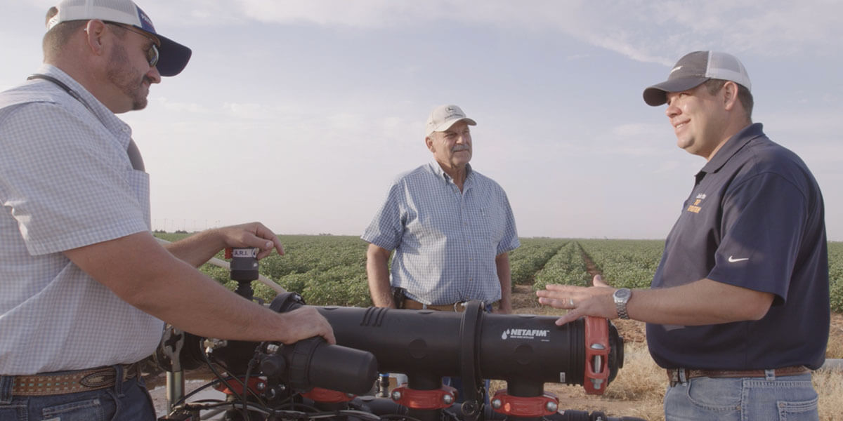 Three farmers discussing irrigation equipment in a sunny field