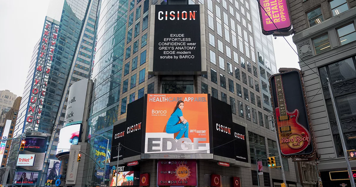 Times Square Cision billboard displays Barco ad showcasing healthcare apparel with a model in blue