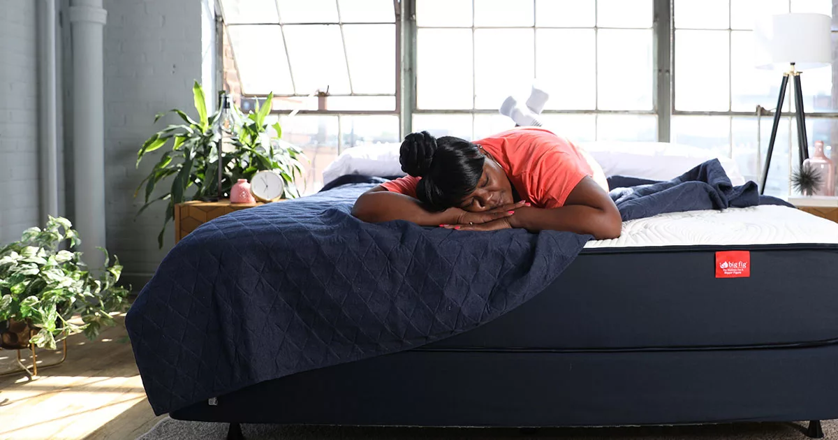 Woman sleeping on a Big Fig mattress in a sunlit room with plants