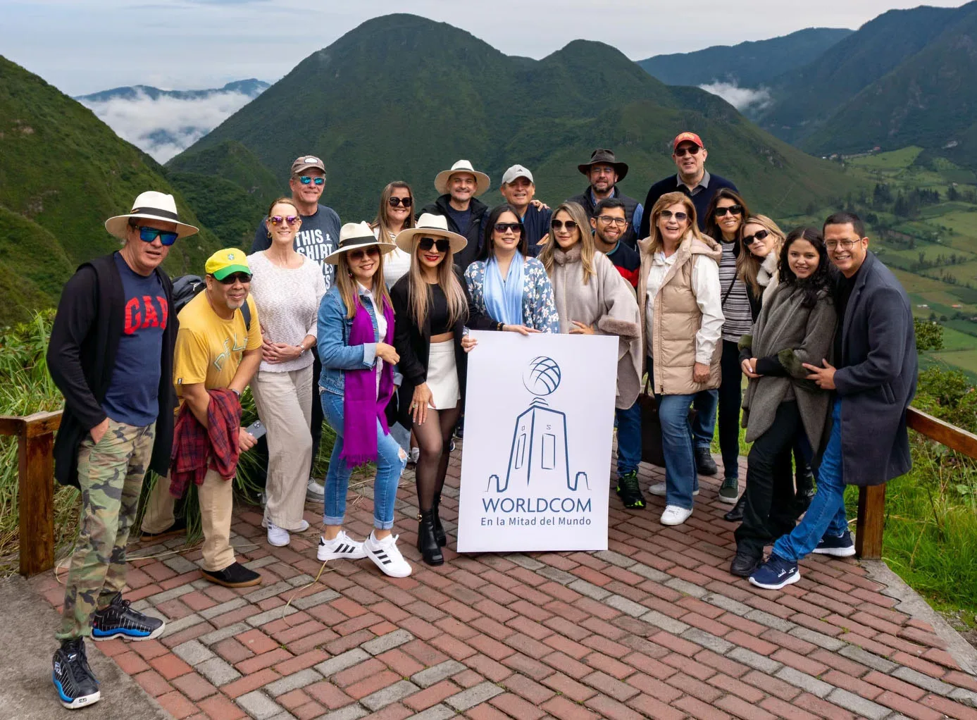 Group of people posing with "Worldcom" sign in front of lush green mountains