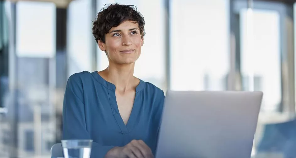 Woman smiling while working at a laptop in a bright office.