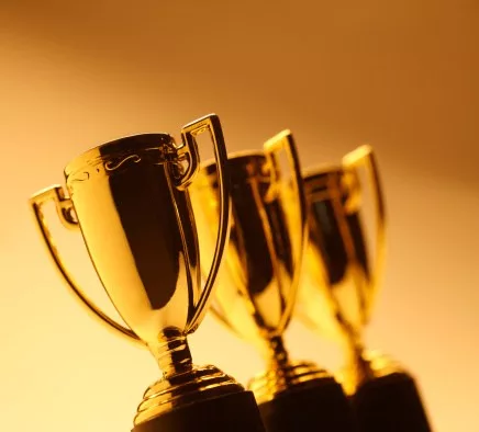 Three gleaming gold trophies in a row against a warm