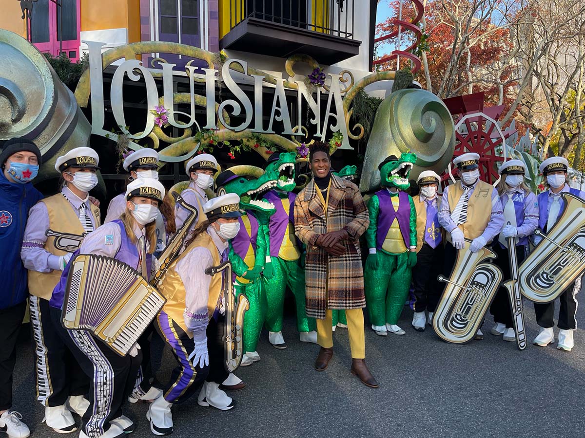 Marching band in festive attire poses with Louisiana float and alligator mascots in parade