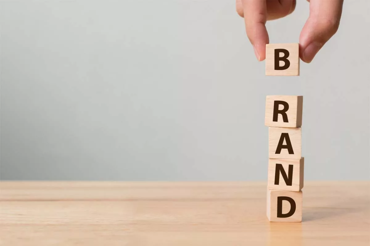 Hand stacking wooden blocks spelling "BRAND" on a wooden surface.