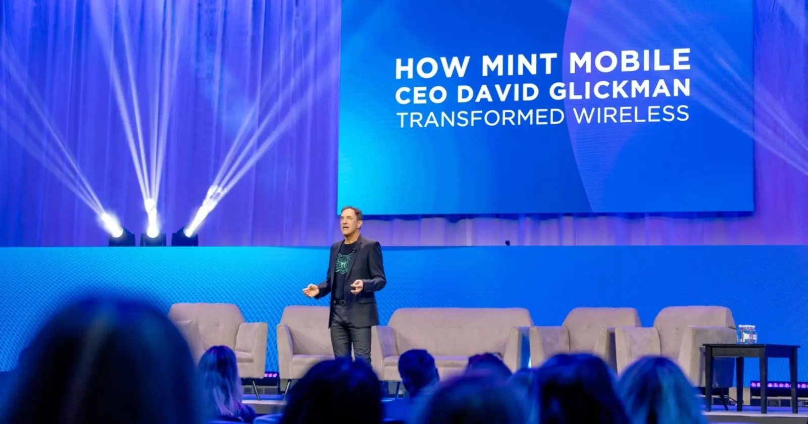 David Glickman speaks on stage about transforming wireless with Mint Mobile at a tech conference, with vibrant lighting.