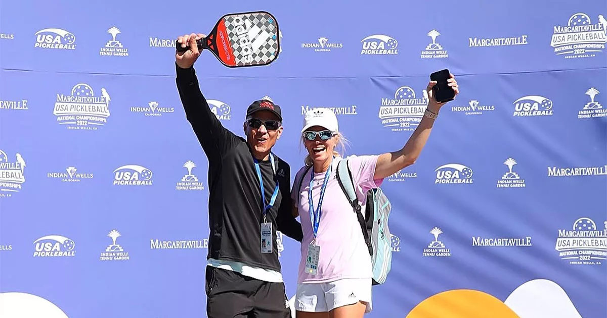 Two pickleball players celebrate in front of USA Pickleball Championship banner with paddles and lanyards.