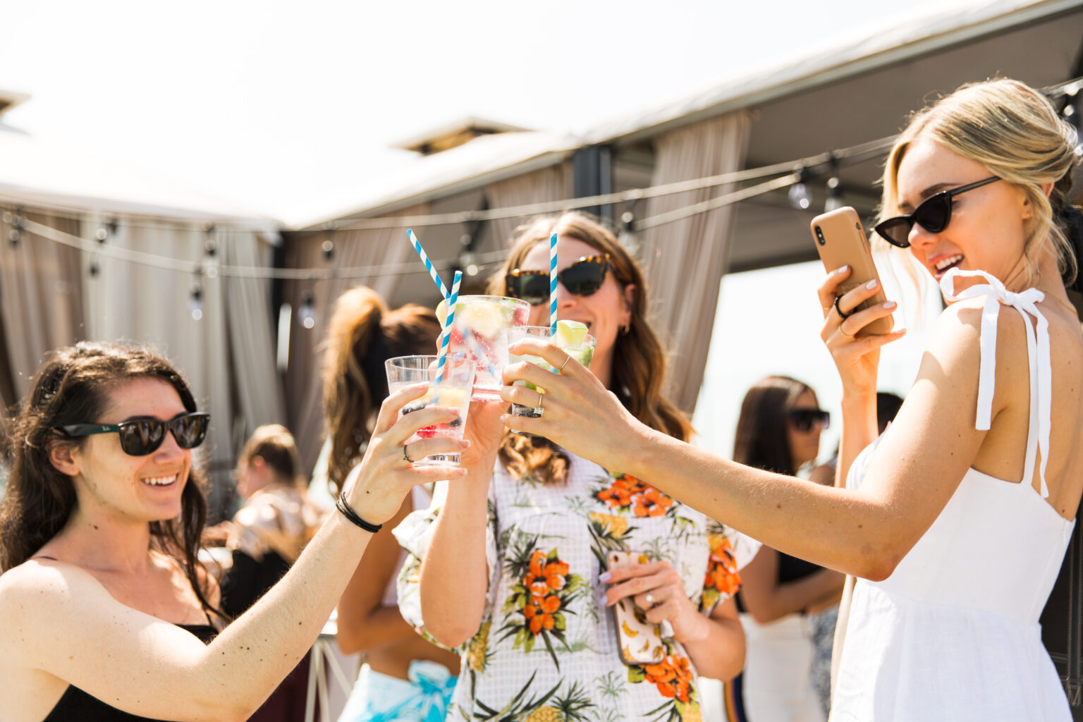 Women in sunglasses clinking colorful drinks at outdoor party