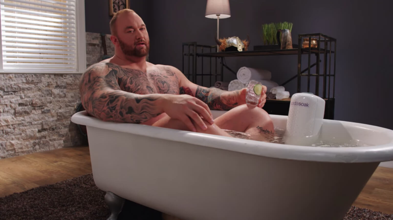 Man with tattoos relaxing in bathtub holding a drink