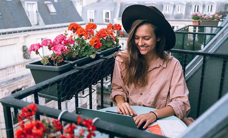 Woman working on laptop at a balcony with colorful flowers