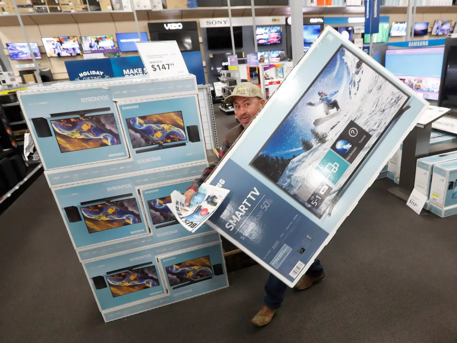 Man carrying large Samsung Smart TV box in electronics store aisle