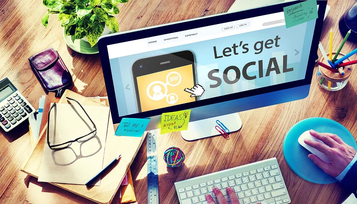 Office desk with a computer displaying "Let's get social" beside glasses