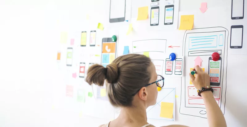 Woman sketching smartphone app design on whiteboard with colorful wireframes and sticky notes
