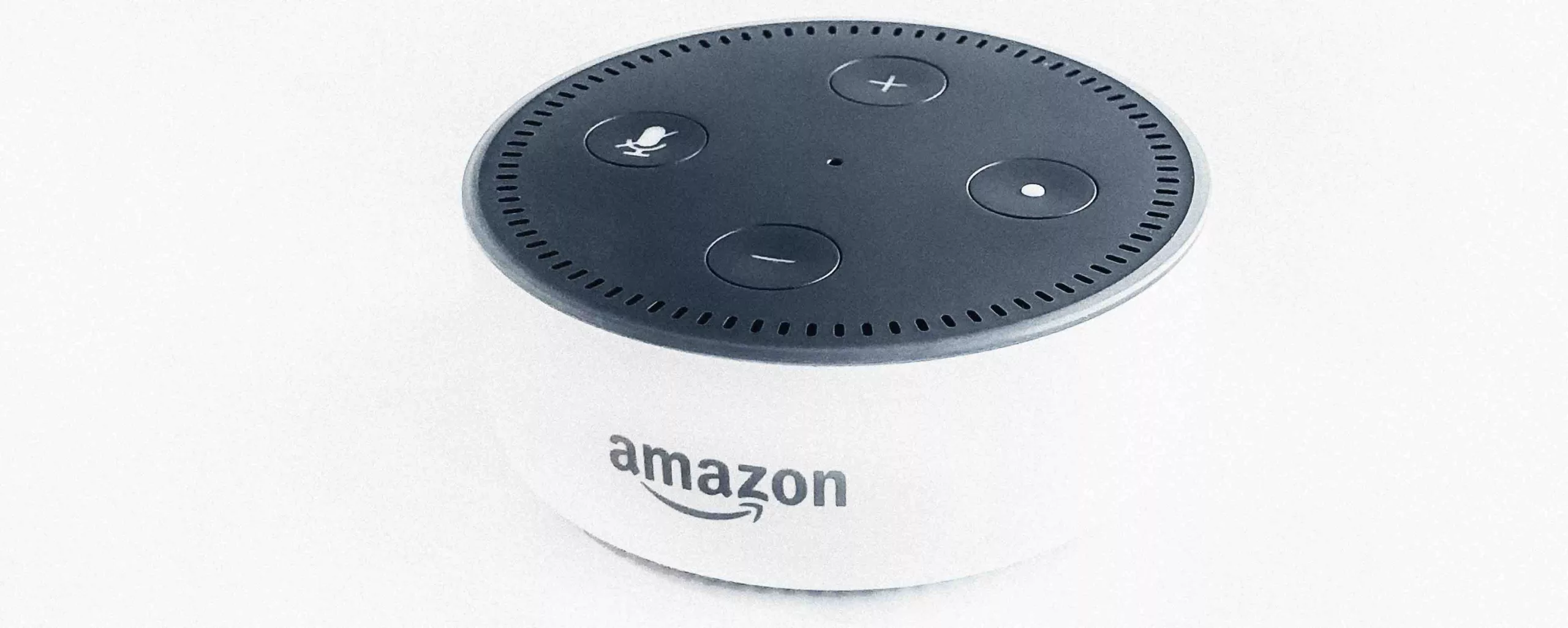 Round smart speaker with a dark top featuring control buttons and a white side with Amazon logo.